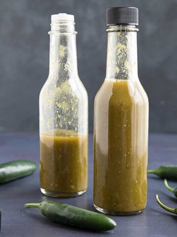 Spicy Serrano Hot Sauce presented in two bottles with peppers around them