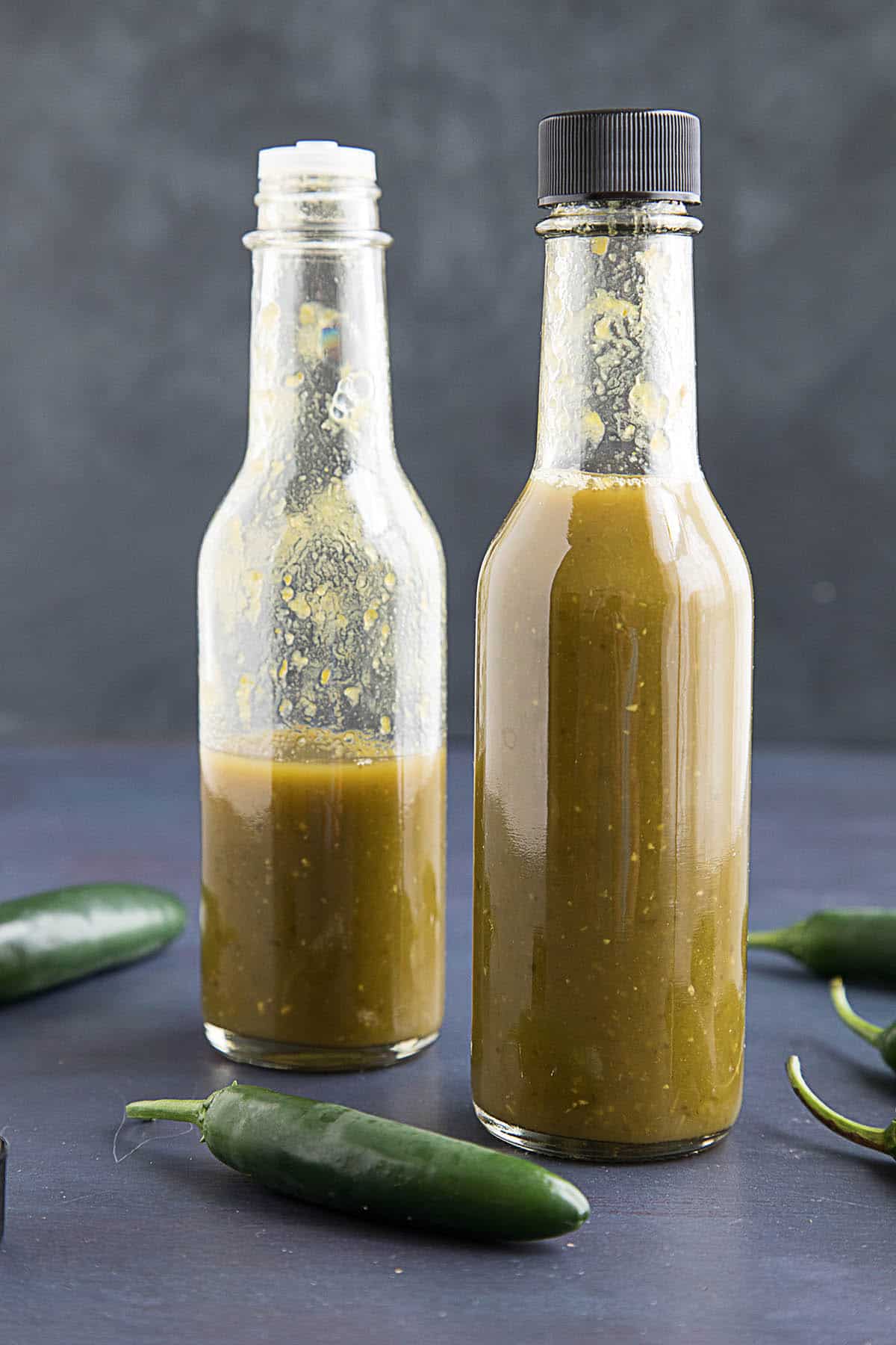 Spicy Serrano Hot Sauce presented in two bottles with peppers around them