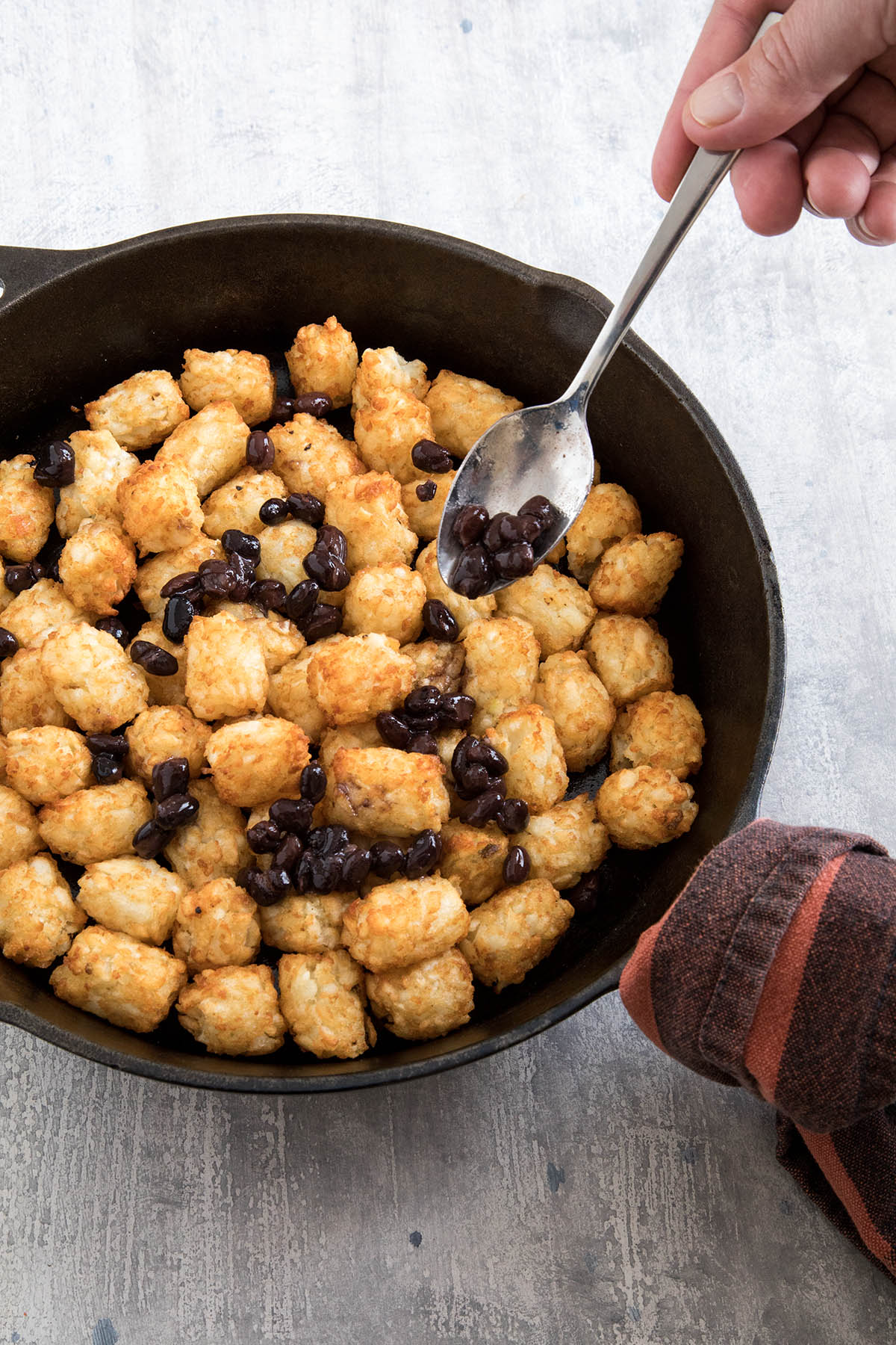 Adding beans when making Cheesy Game Day Totchos (Tater Tot Nachos).