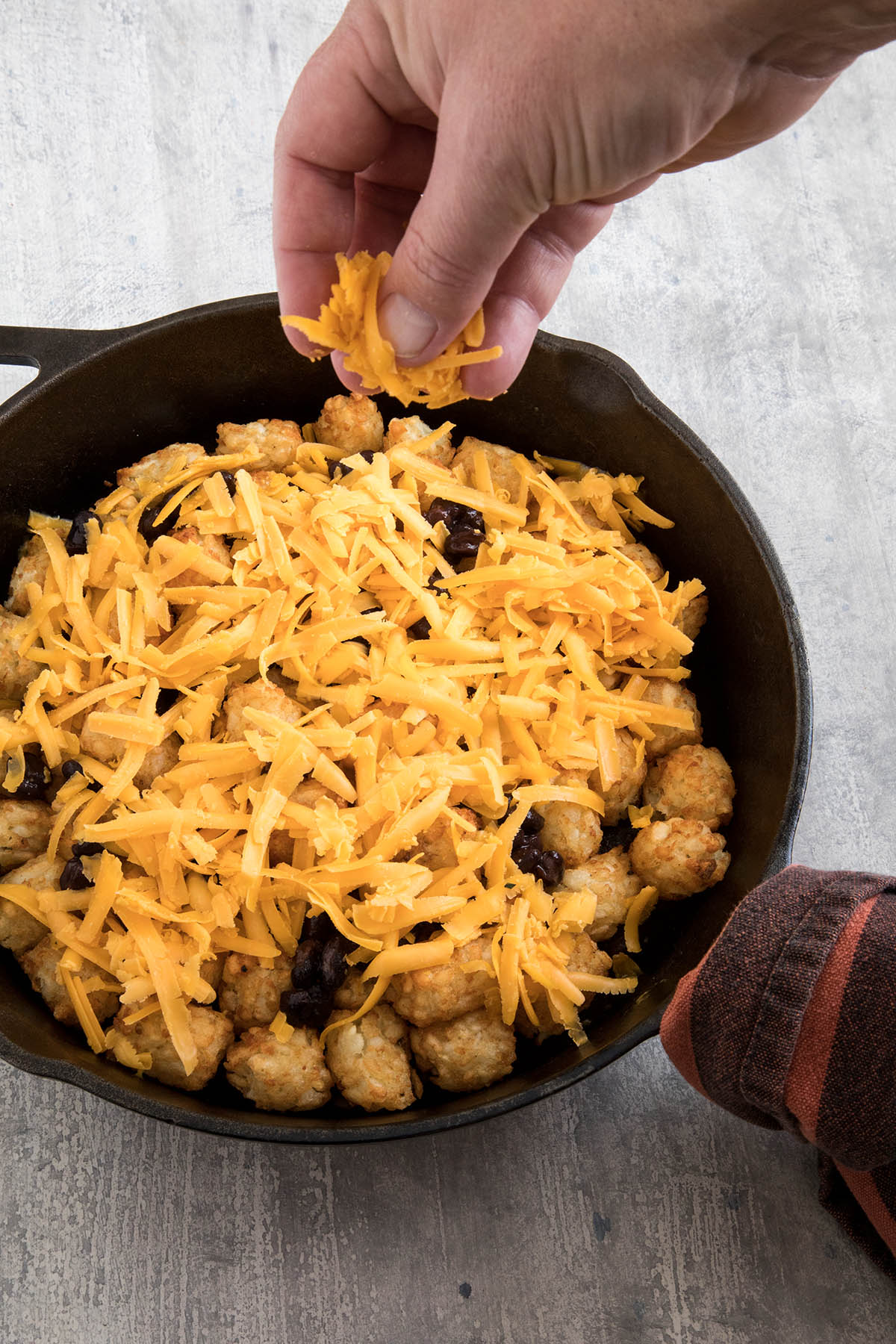 Adding cheese, making Game Day Totchos (Tater Tot Nachos).