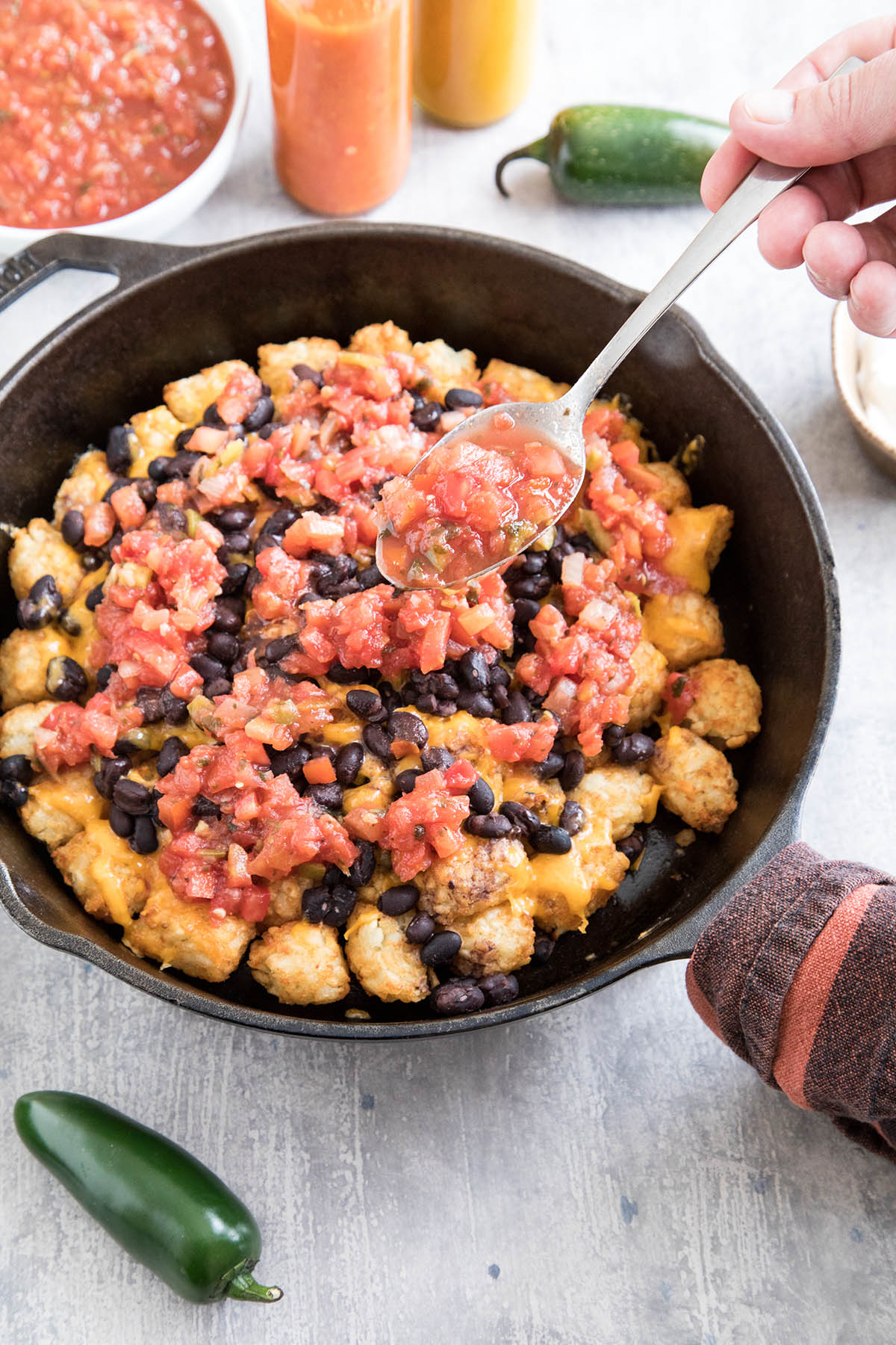 Adding salsa to the skillet, making cheesy Game Day Totchos (Tater Tot Nachos).