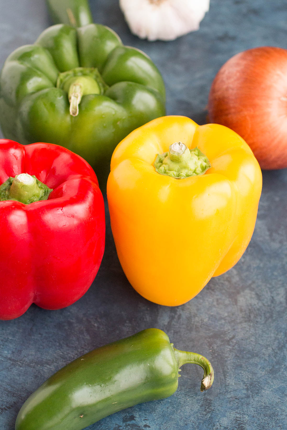 Bell peppers of three colors with an onion next to them.