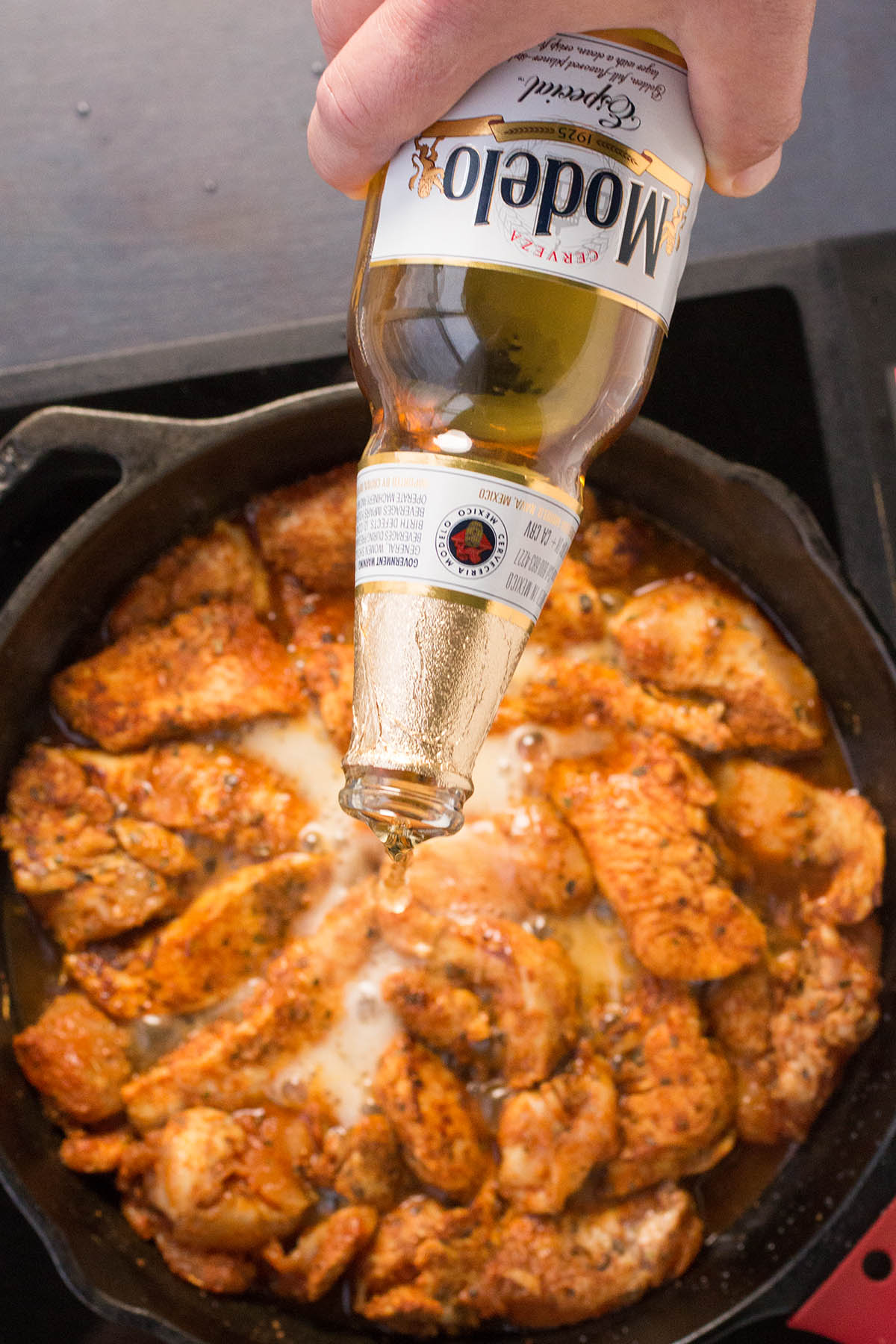 Pouring beer into the chicken in the skillet.