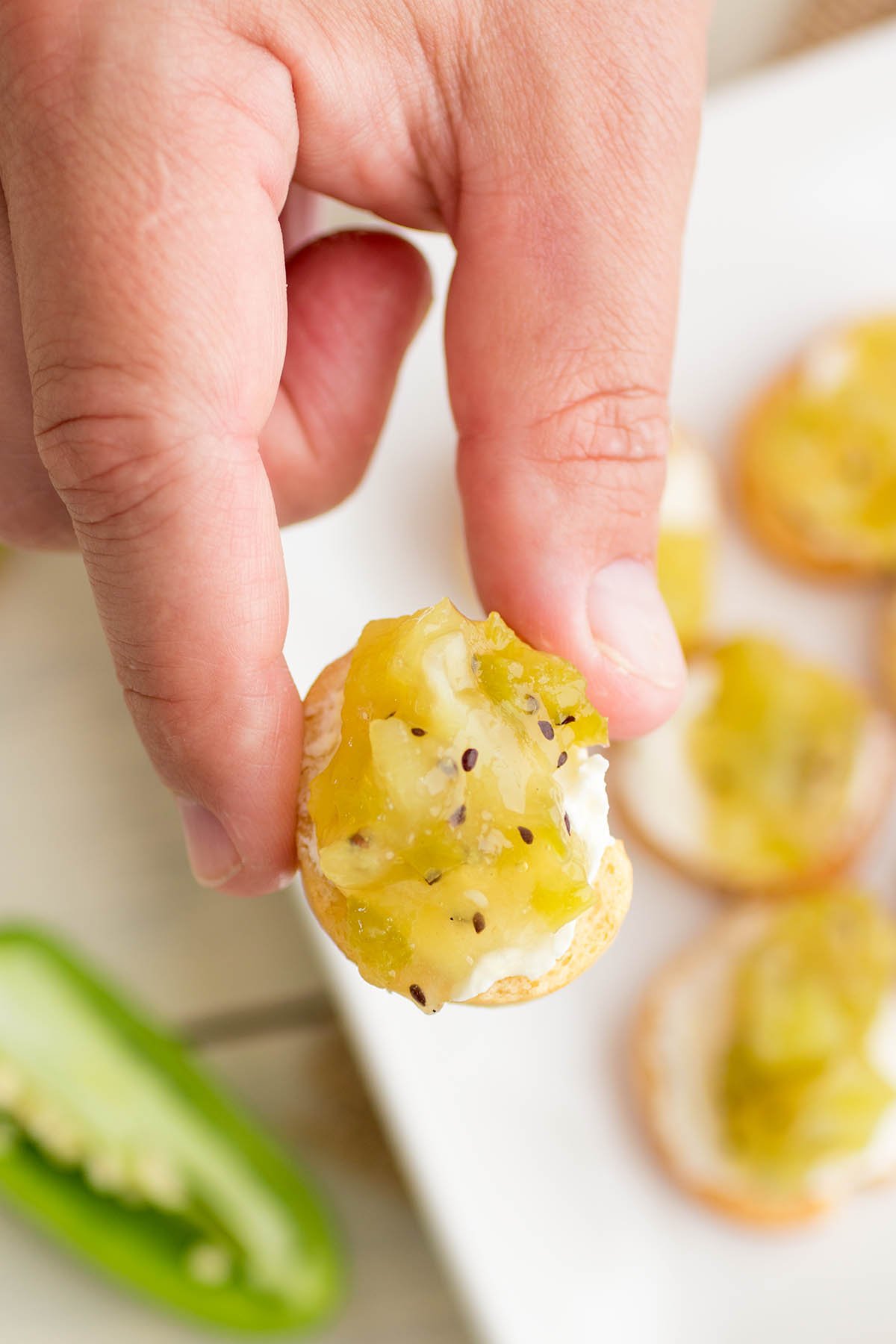 Holding a tiny toast bite with Kiwi-Jalapeno Jam on top