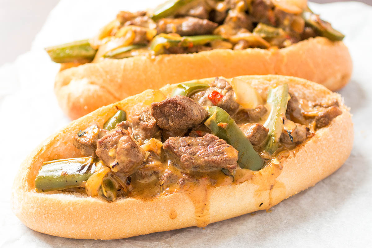 Two mouthwatering Mexi Cheesesteak Sandwiches on a piece of parchment paper