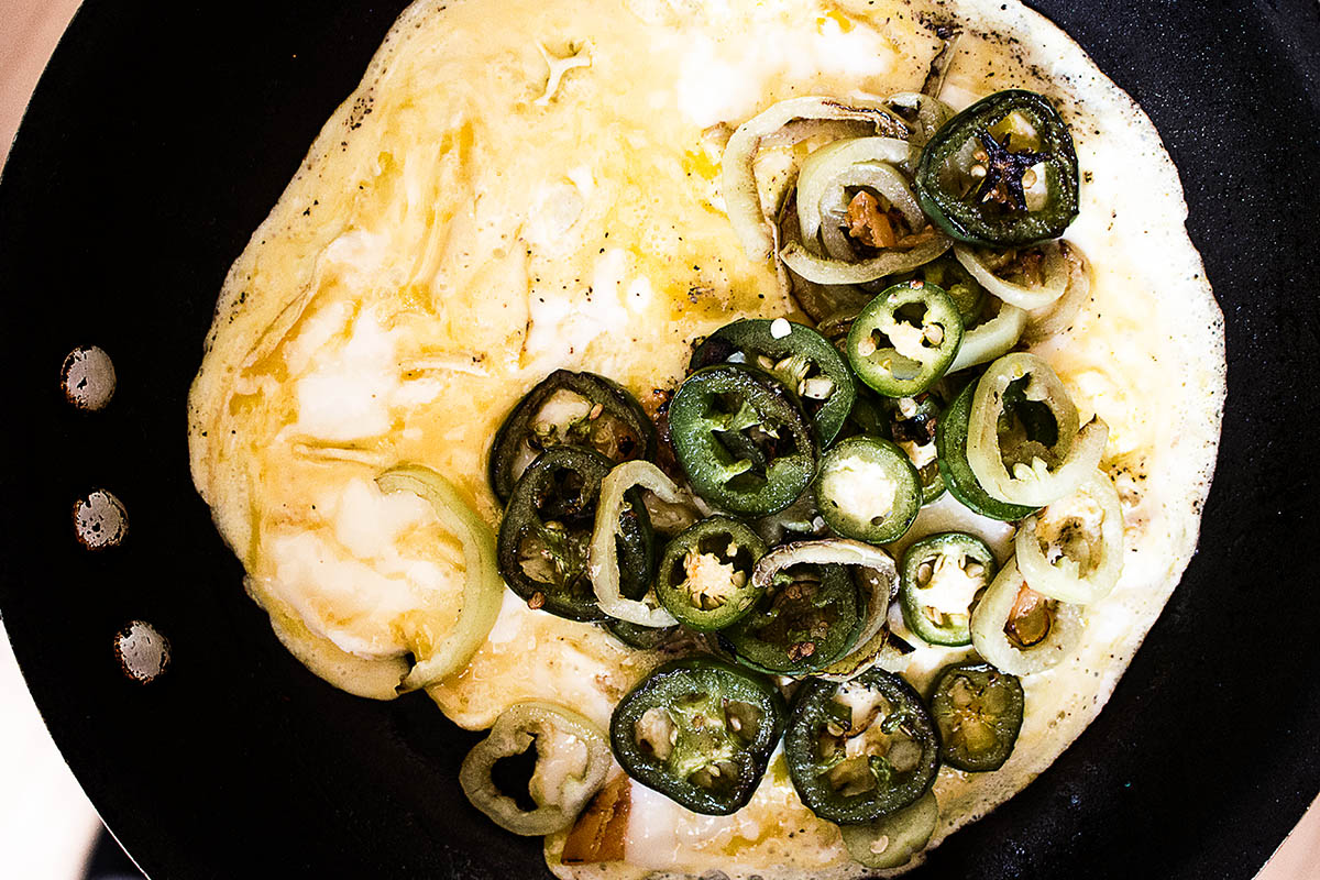 Adding eggs to the peppers in the skillet