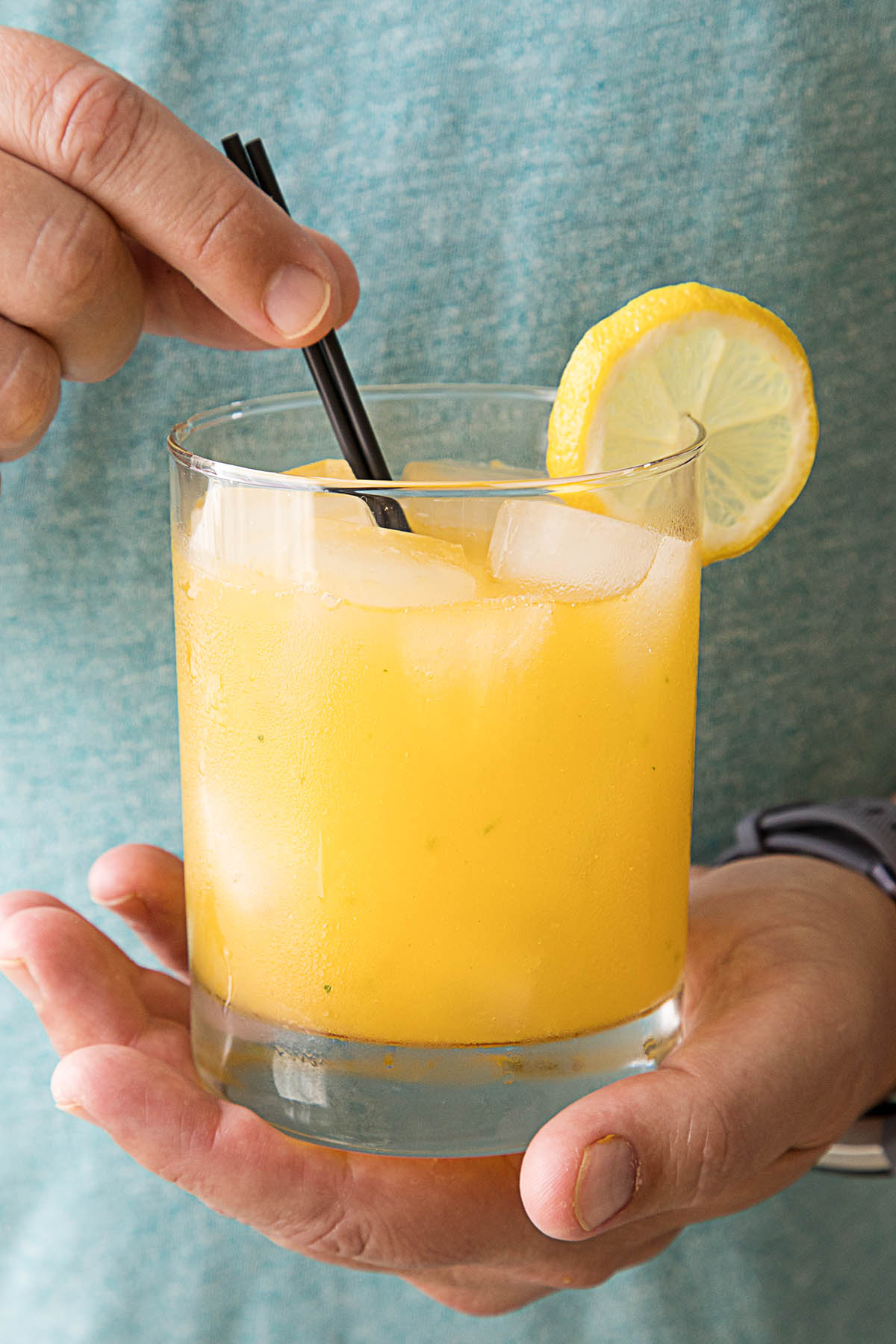 Holding a glass of the Fiery Mango-Habanero Cocktail in two hands.