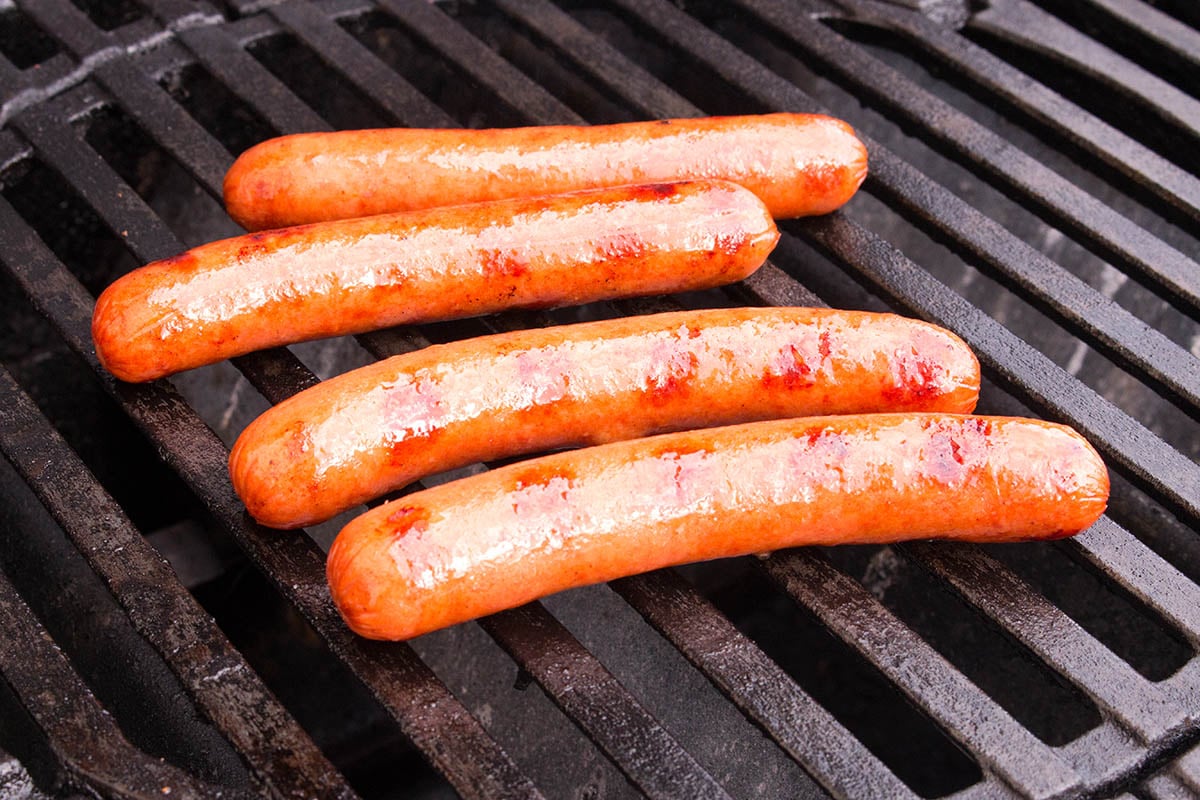 Preparing sausages on a grill for nacho cheese dog.