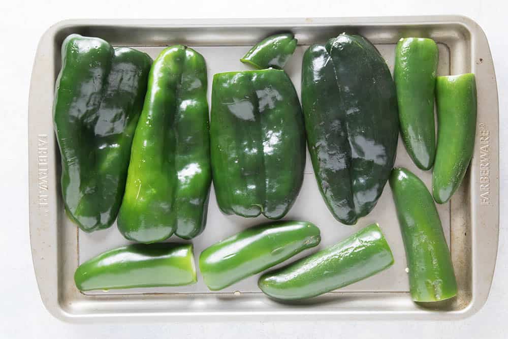 Poblano peppers and jalapeno peppers, sliced and on a baking sheet, ready to roast