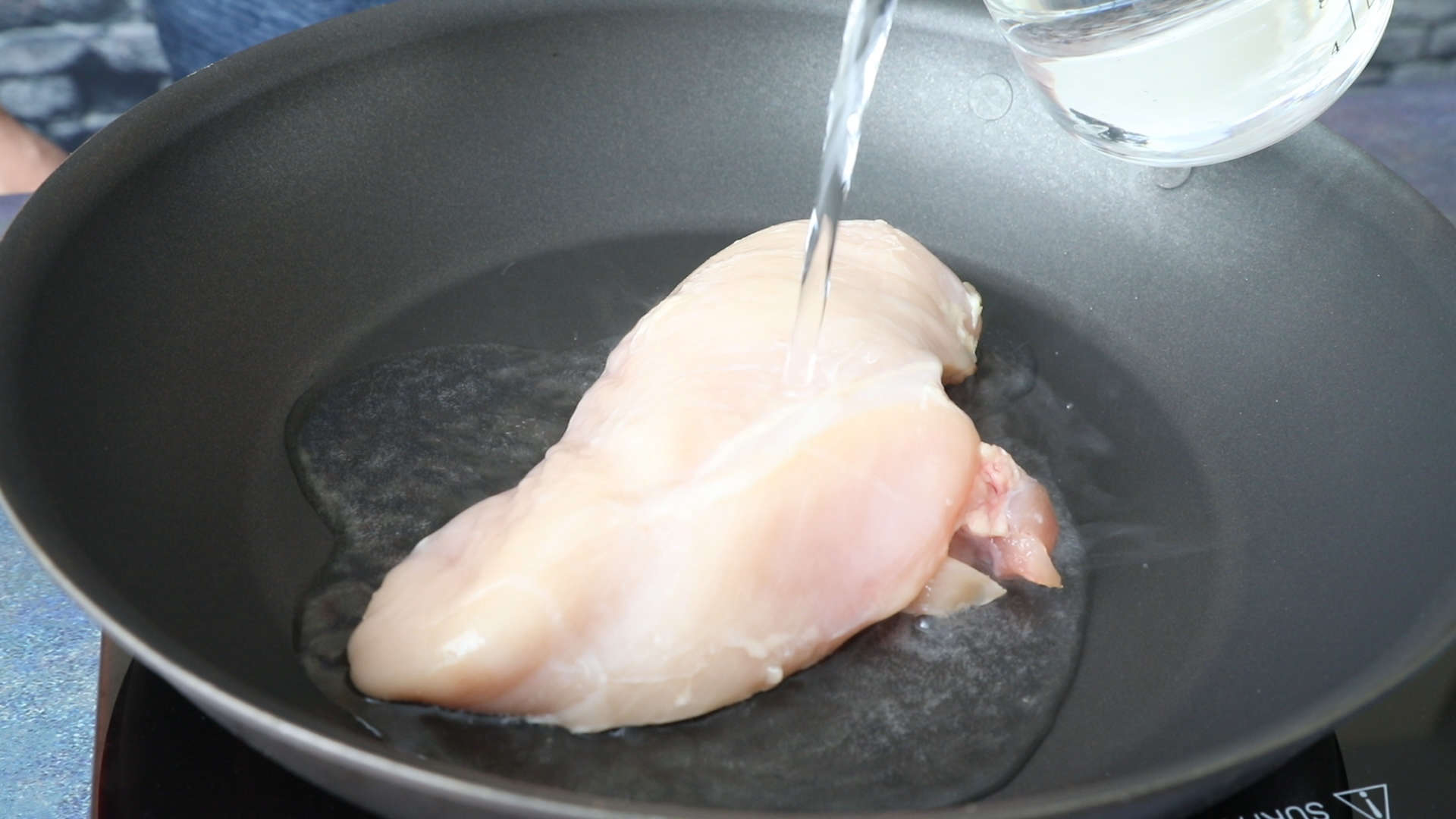 Poaching a chicken breast in a pan.