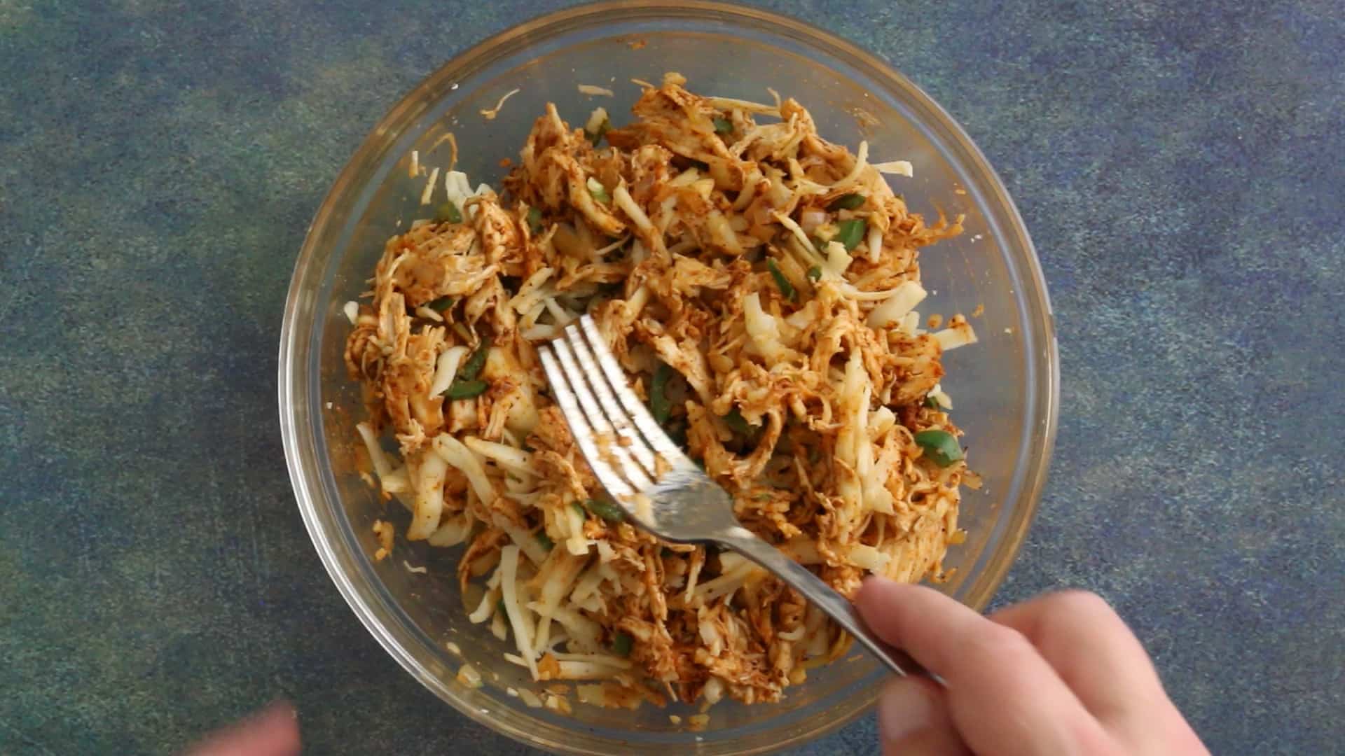 Mixing the seasoned shredded chicken with cheese.