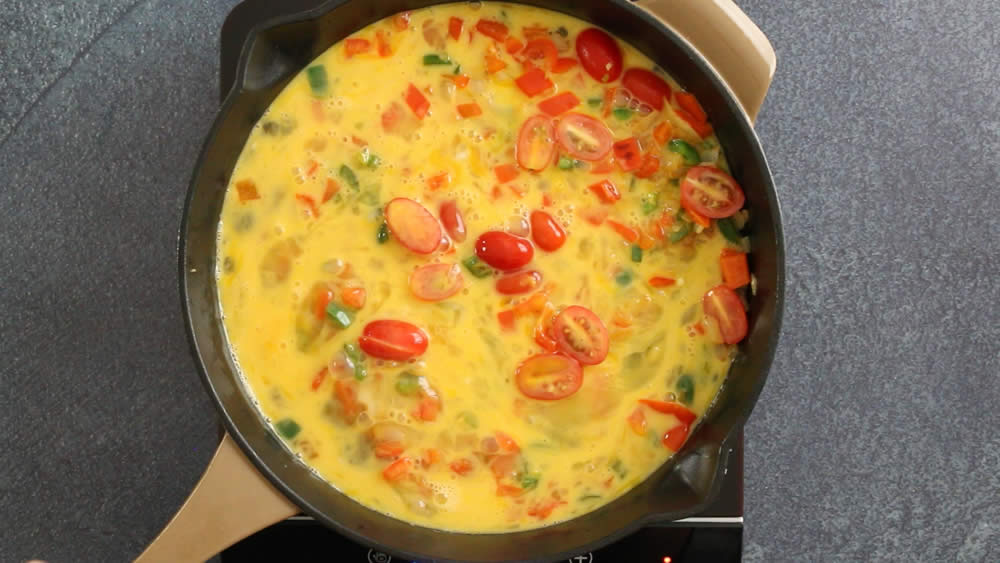 Freshly poured scrambled eggs, heating in a pan with tomatoes, onion and peppers.