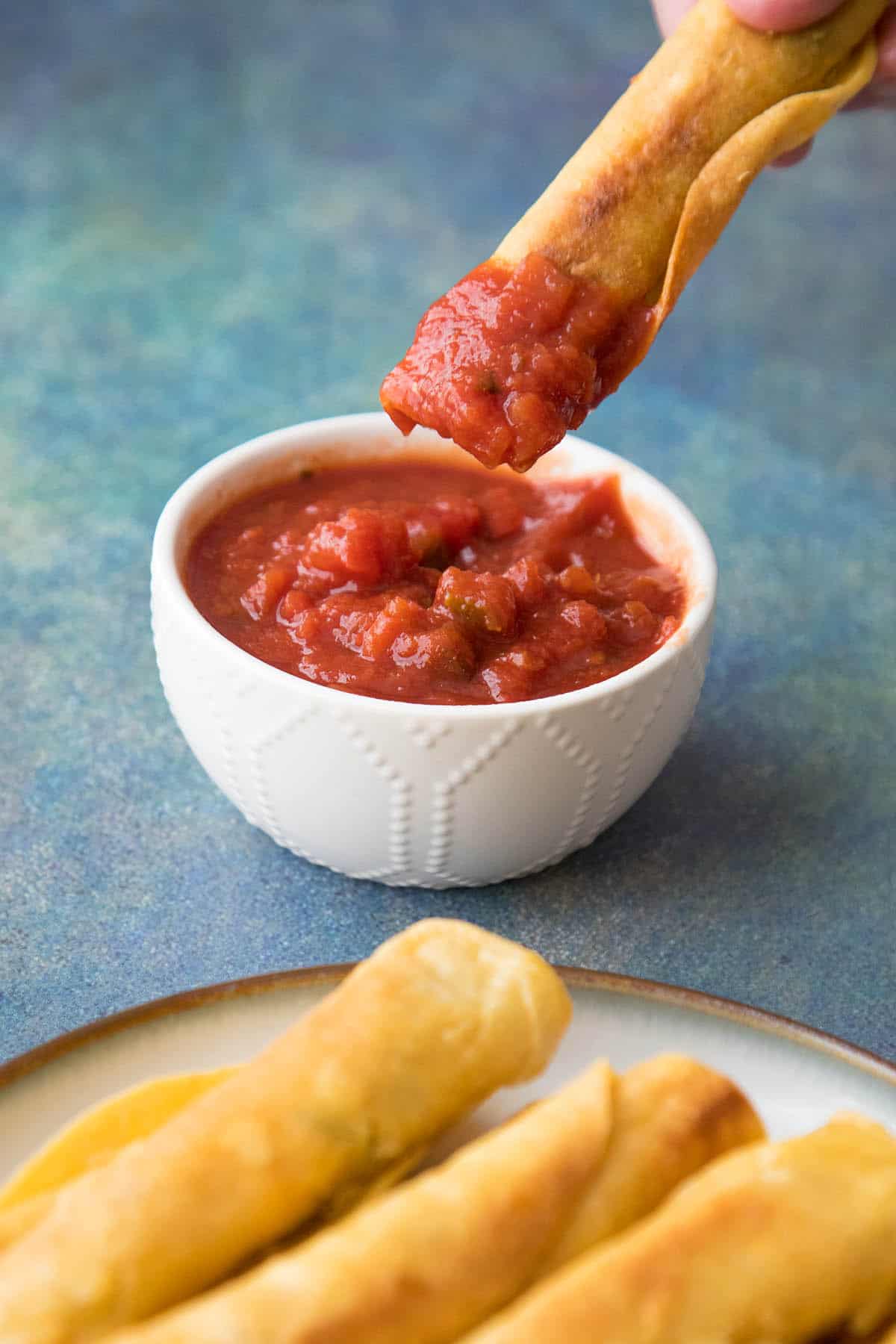 Chicken Taquitos dipped in salsa.