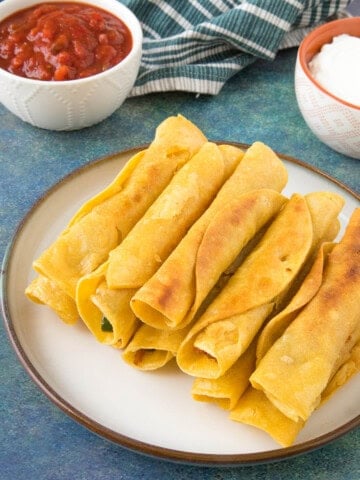 Chicken Taquitos stacked on a plate with salsa.