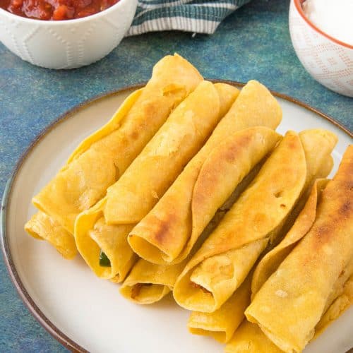 Chicken Taquitos stacked on a plate with salsa.