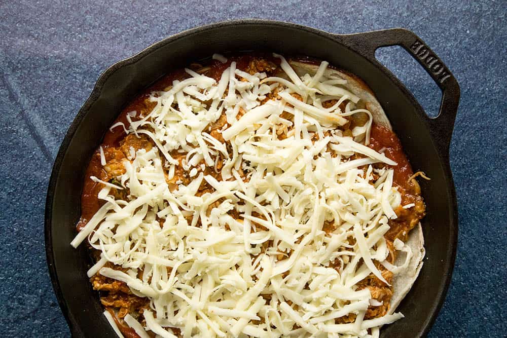 Lots of cheese layered over corn tortillas and chipotle chicken in a pan