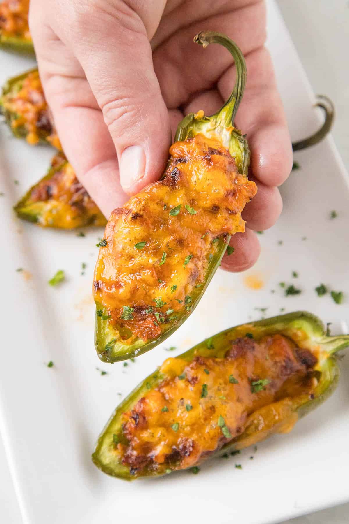 Holding Pulled Pork-Sriracha Jalapeno Poppers in the right hand.