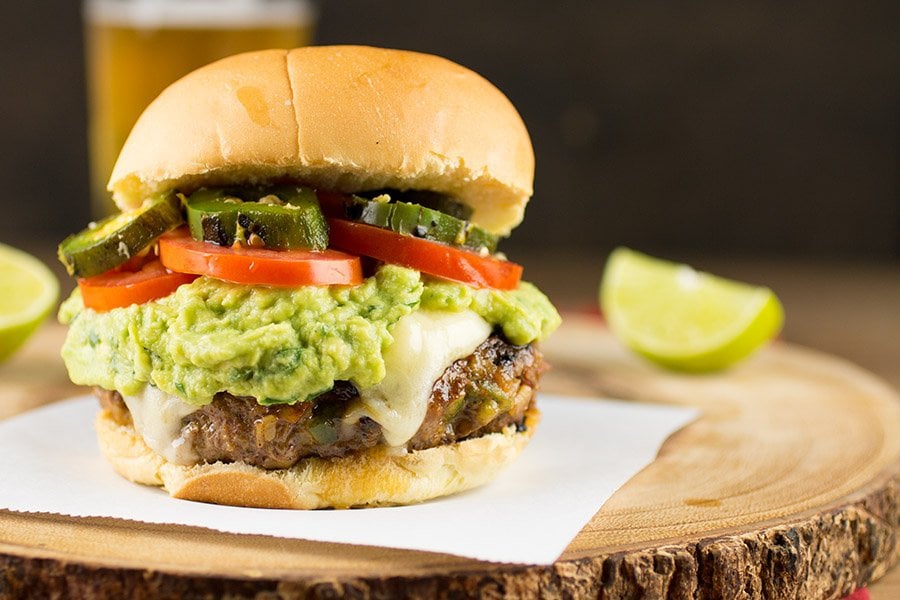 Mexican Burger on a platter, ready to eat, with lots of cheese, guacamole and roasted jalapeno peppers