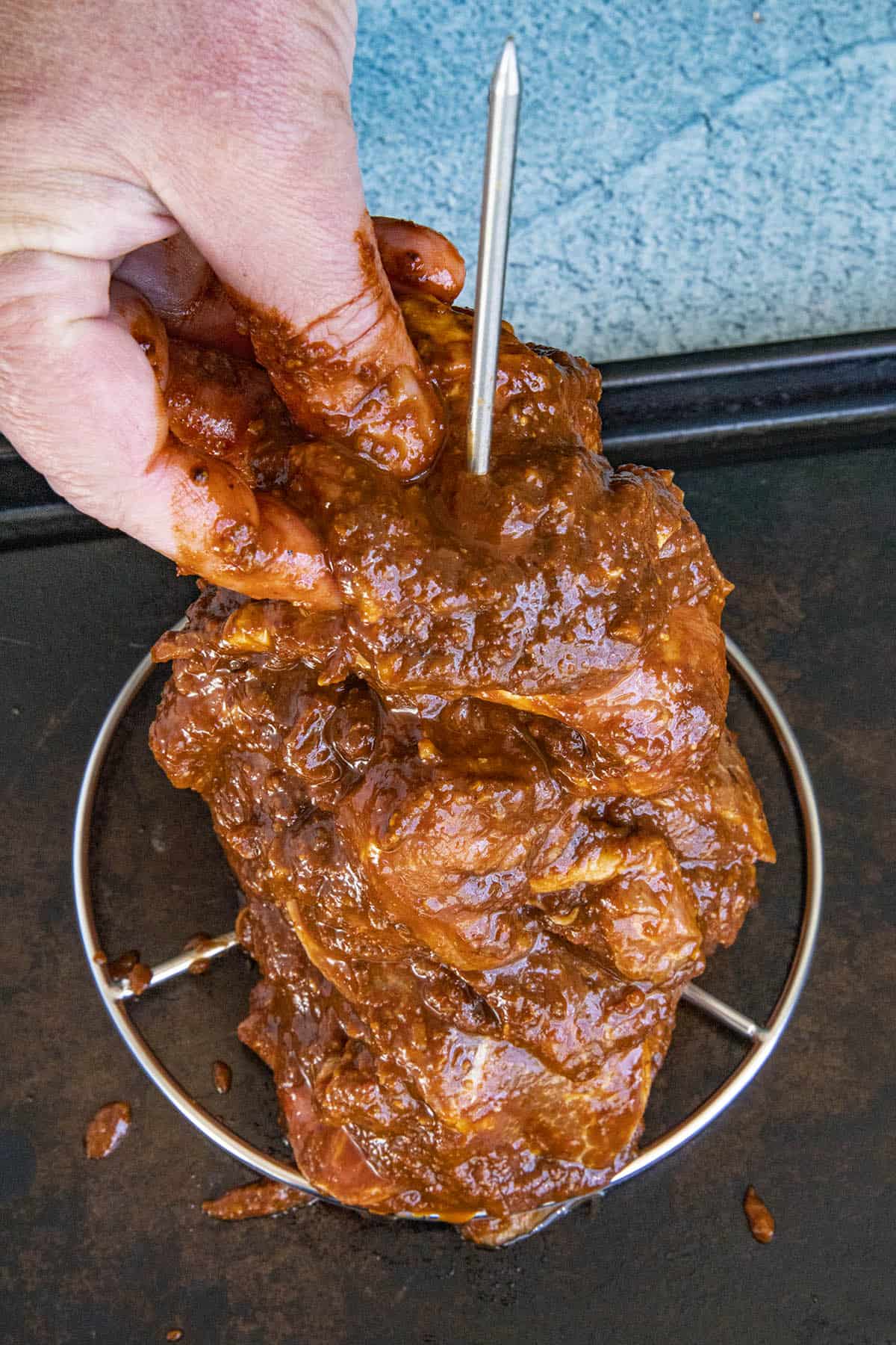 Adding marinated pork shoulder to the vertical skewer