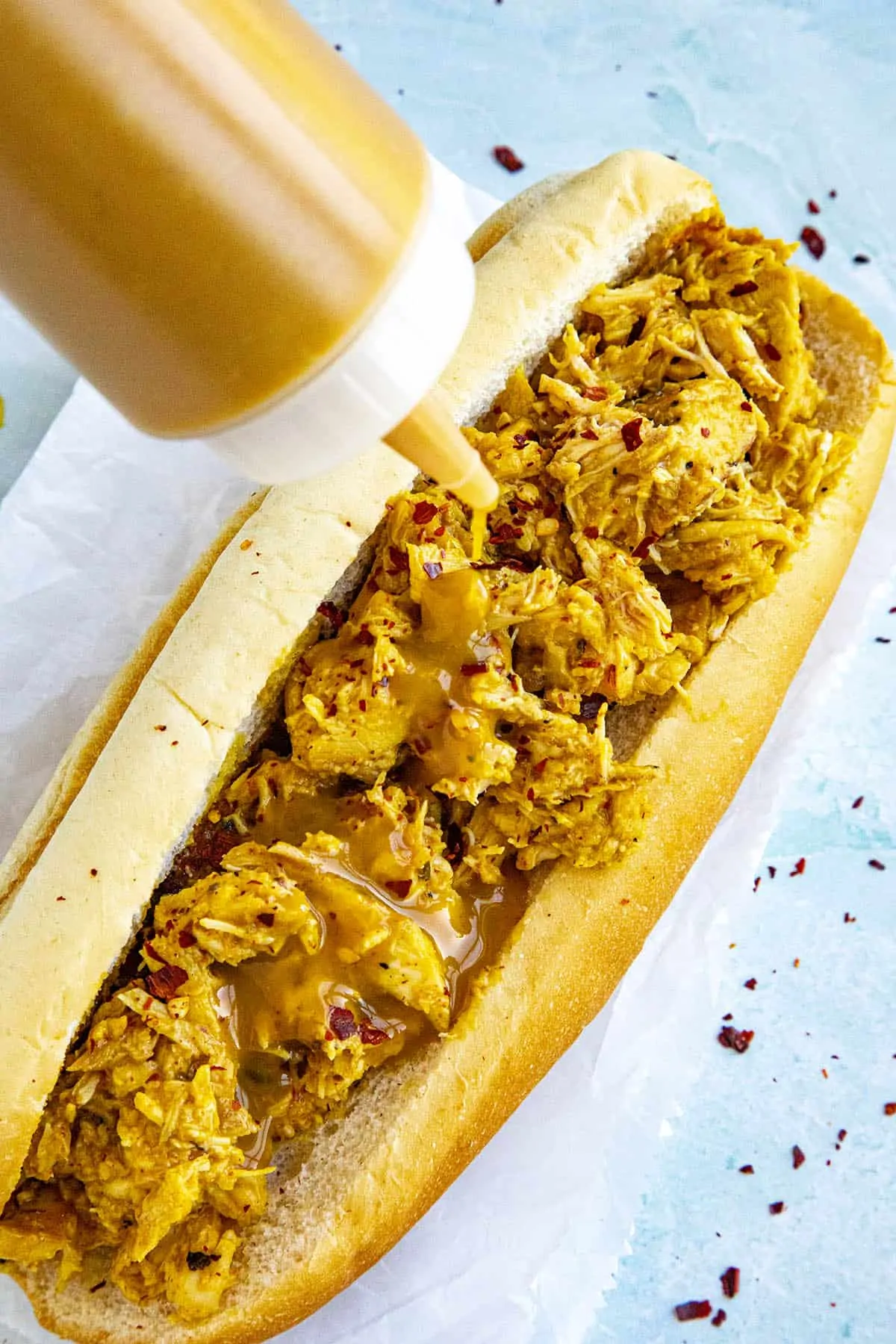 Carolina Mustard BBQ Sauce being squirted onto a pulled chicken sandwich