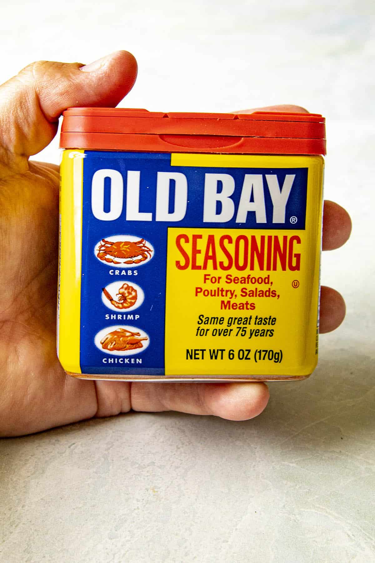 Holding Old Bay Seasoning in the left hand.