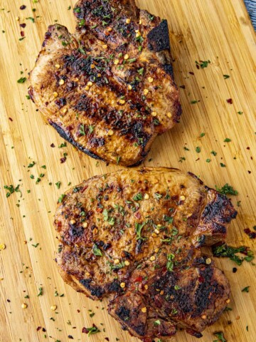 Two juicy bone-in grilled pork chops on a cutting board