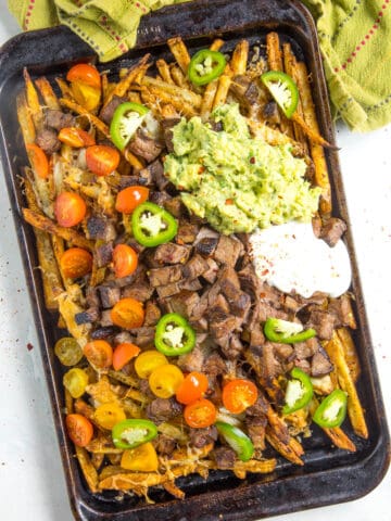 Carne Asada Fries on a baking sheet with lots of fixings