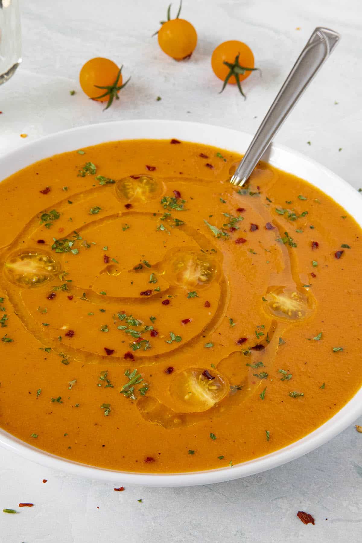 A bowl of Roasted Tomato Soup with spicy chili flakes, sliced cherry tomatoes and a swirl of olive oil on top