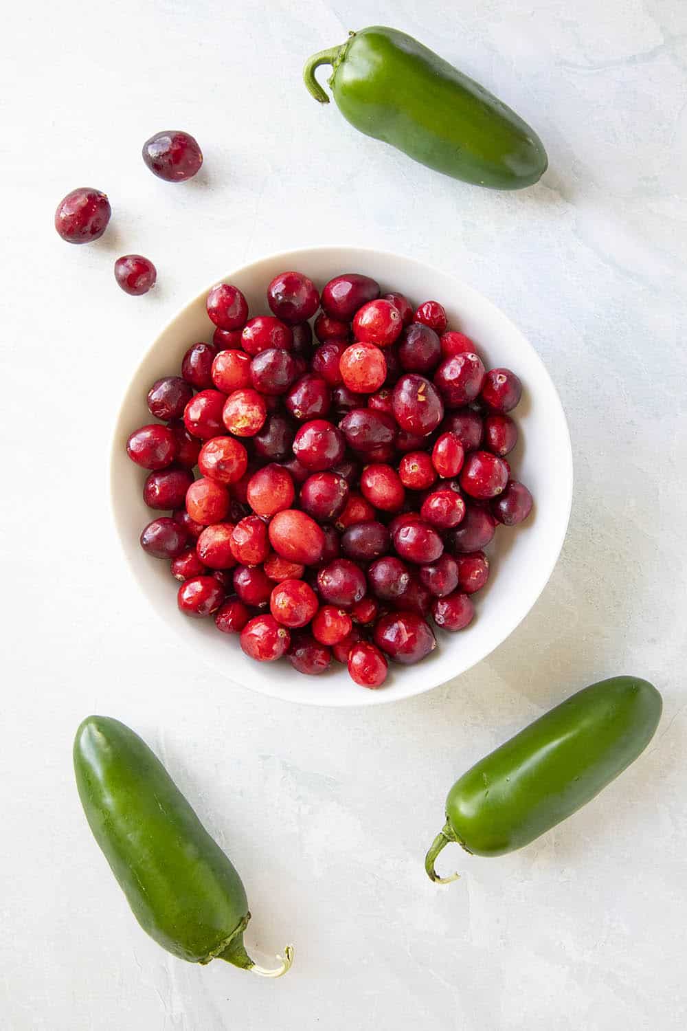 A bowl of cranberries with 3 jalapeno peppers around it