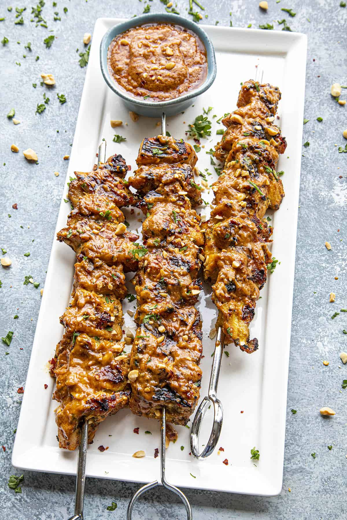 Thai Chicken Satay skewers on a plate, slathered with spicy Thai peanut sauce