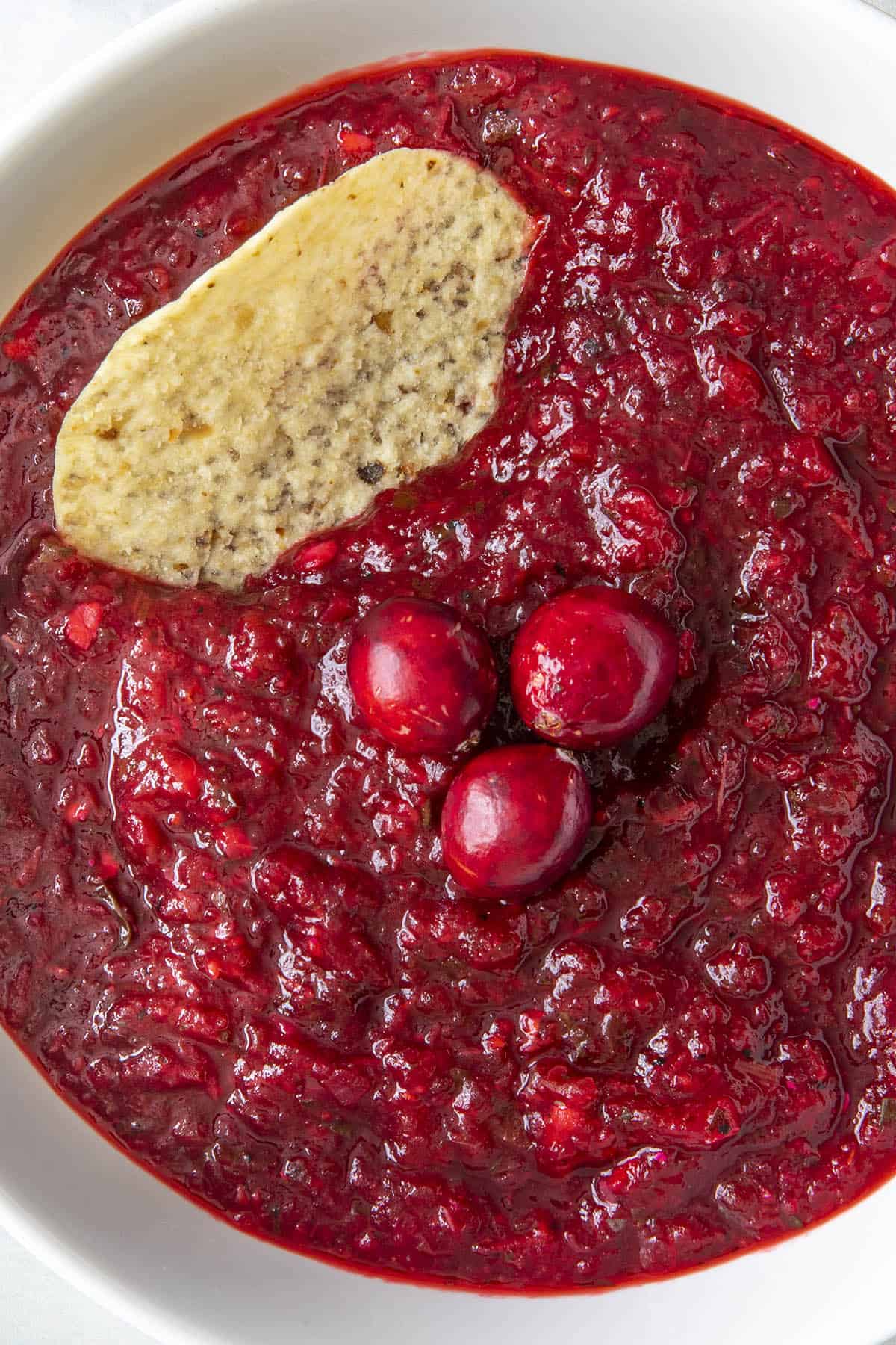 Vibrant, Spicy Cranberry Salsa in a bowl with a chip