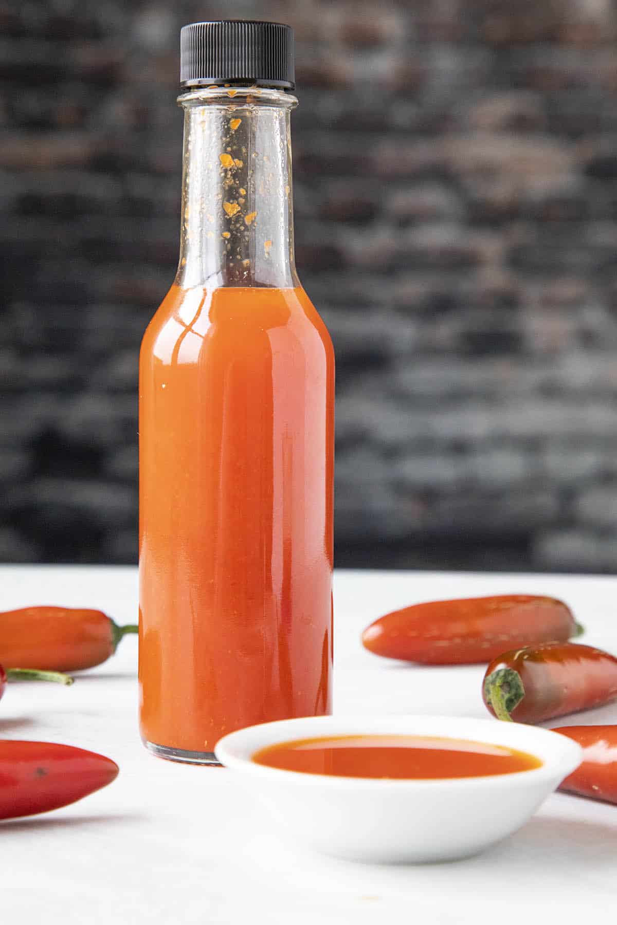 A bottle of Red Serrano Hot Sauce next to a small bowl of the hot sauce