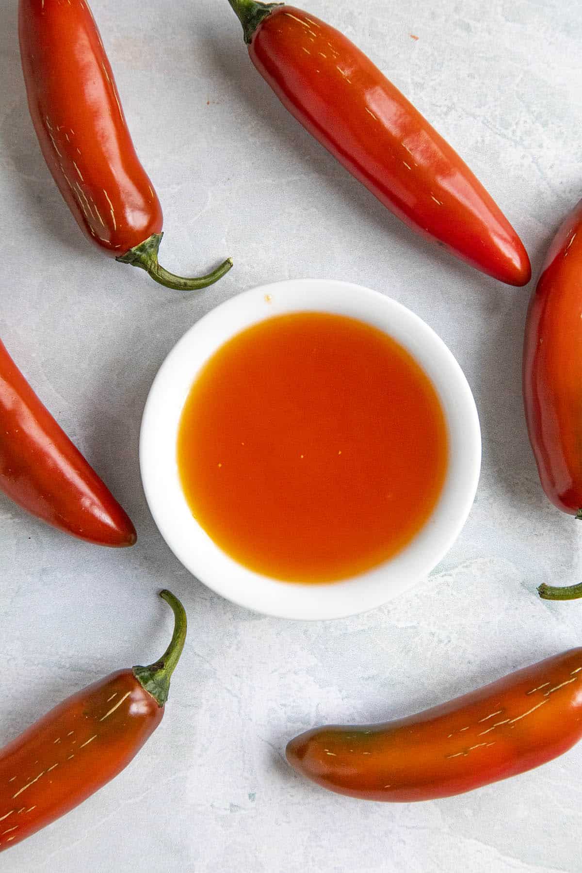 Red Serrano Hot Sauce in a small bowl, surrounded by red serrano peppers