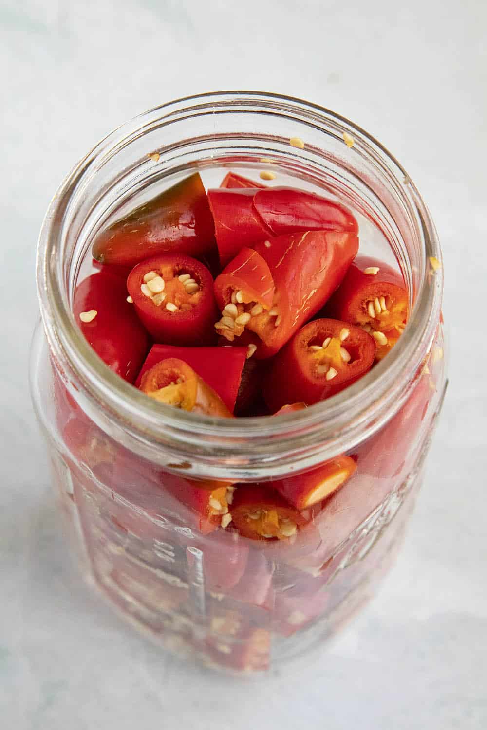 Red serrano peppers stuffed into a jar, ready for the brine to ferment