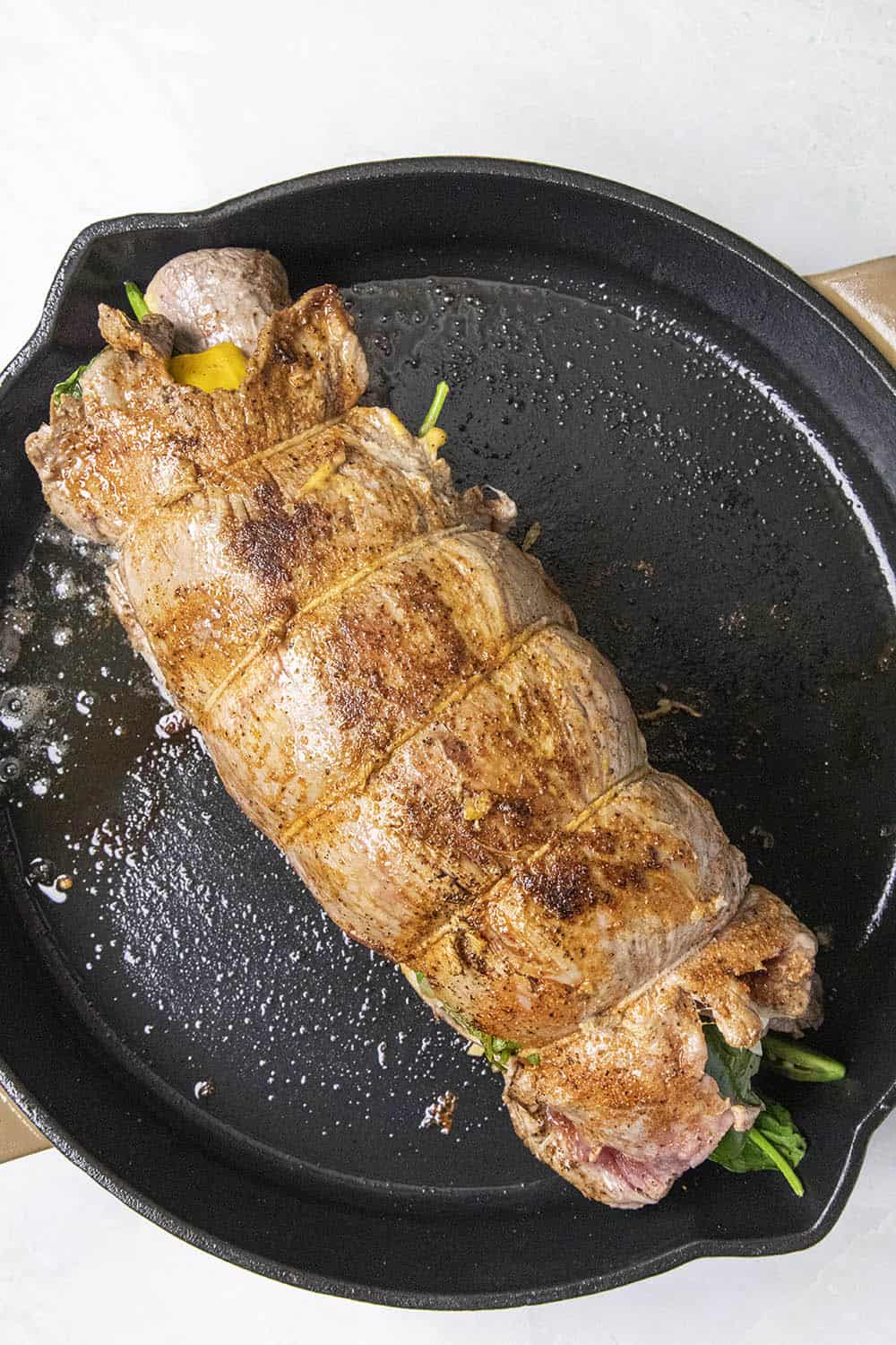 Searing the stuffed flank steak in a hot cast iron pan