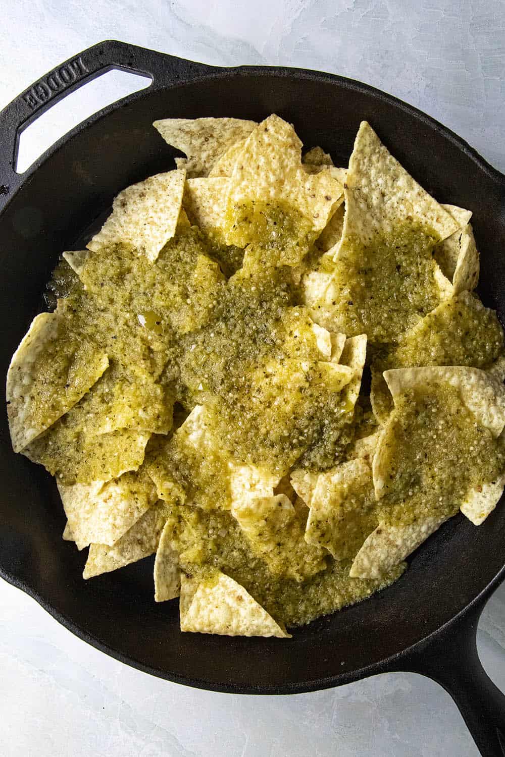 Tortillas in a pan, topped with salsa verde, ready for some fried eggs