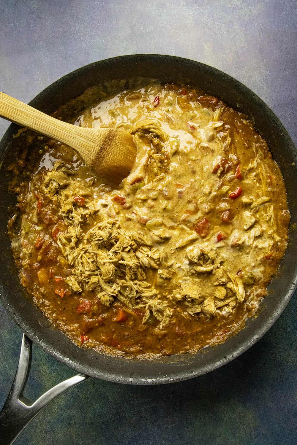 Adding fire roasted tomatoes and sour cream to the vegetables and roux in a pan.