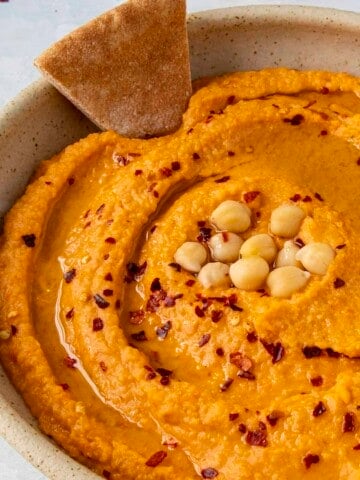 Roasted Red Pepper Hummus with a chip in the bowl