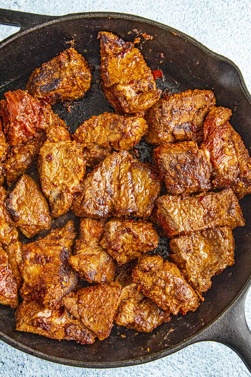 Chunks of seasoned meat seared in a cast iron pan