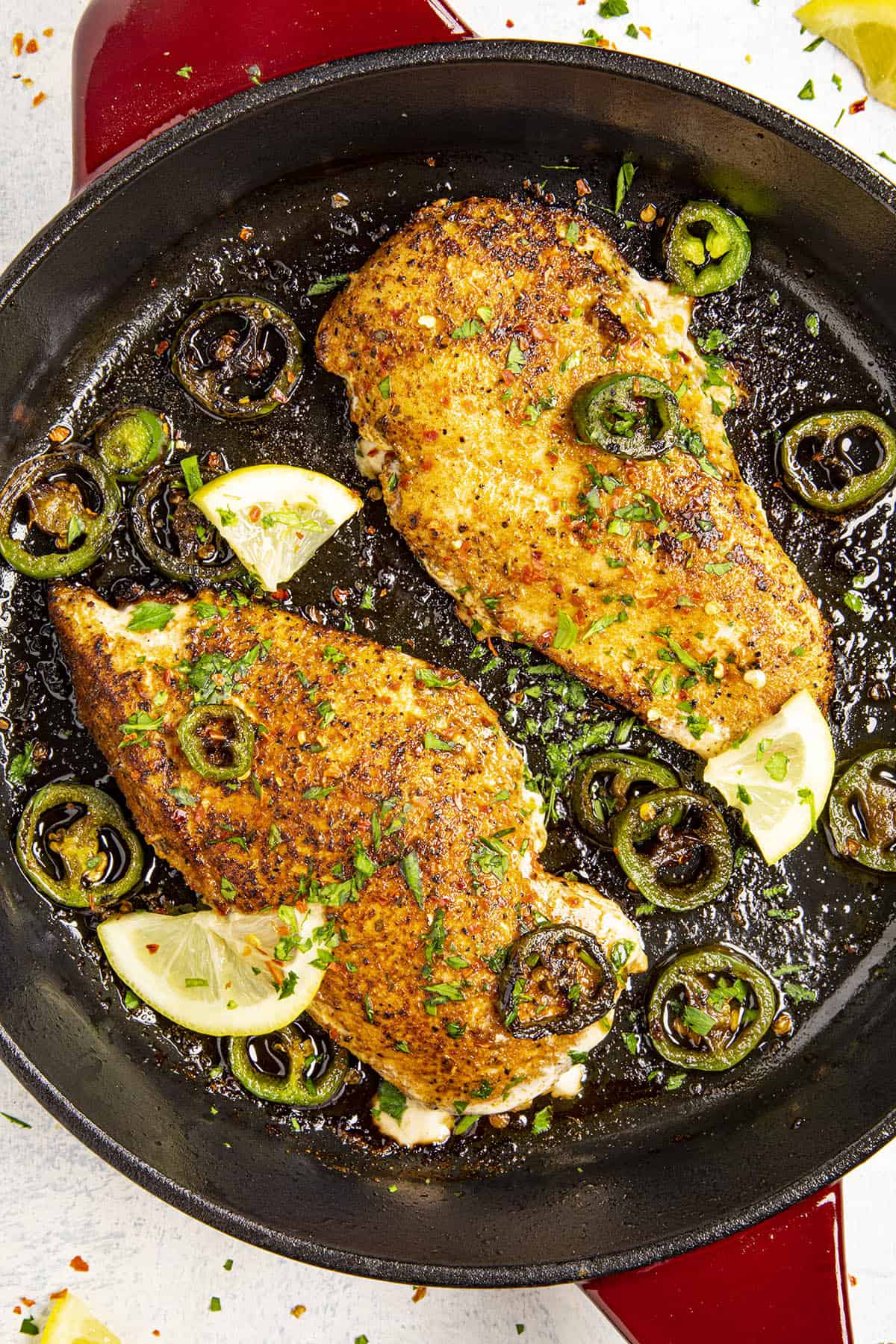 Two Blackened Chicken in a pan with seared jalapenos and lemon slices