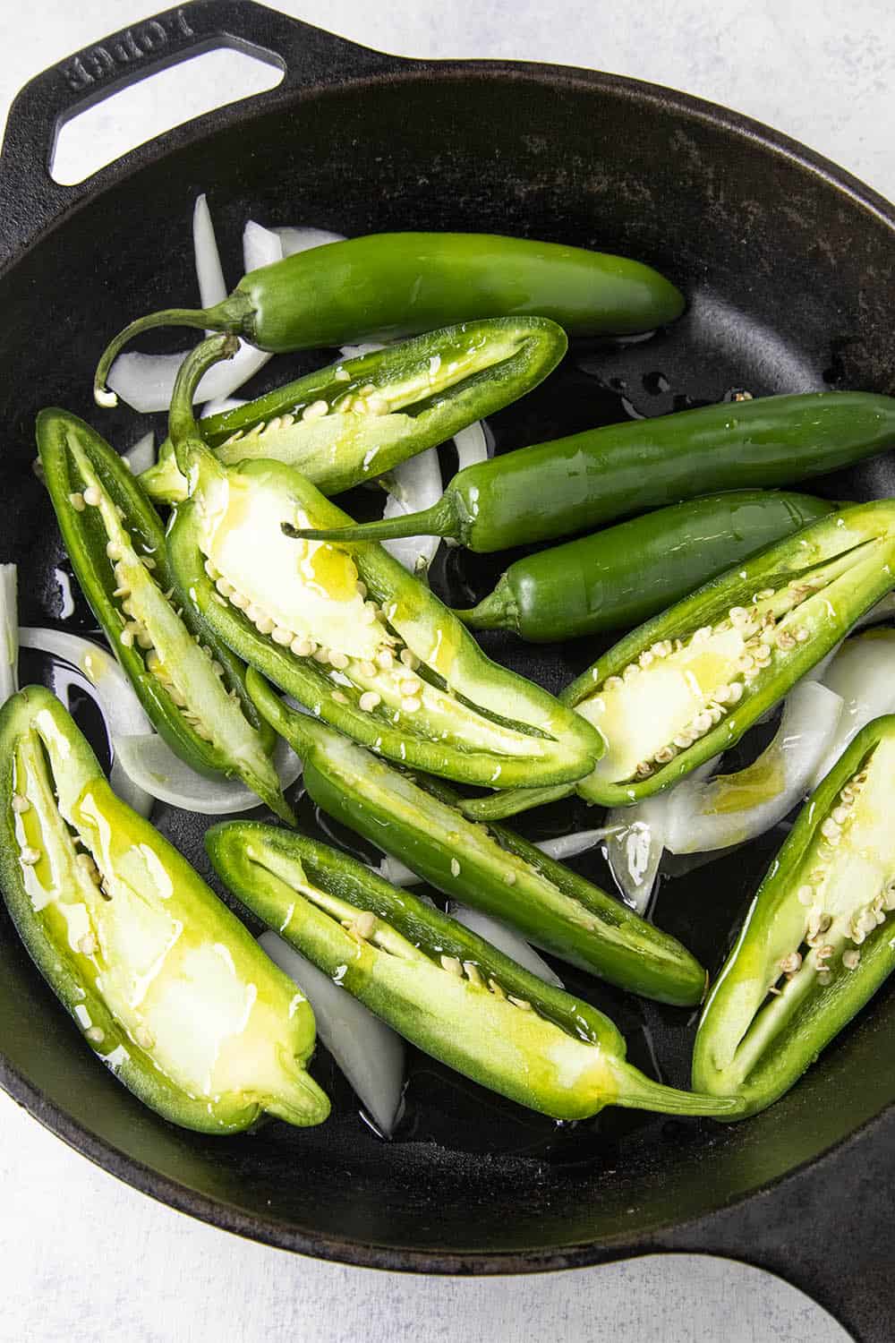 Drizzling olive oil over the jalapeno and serrano peppers in a hot pan