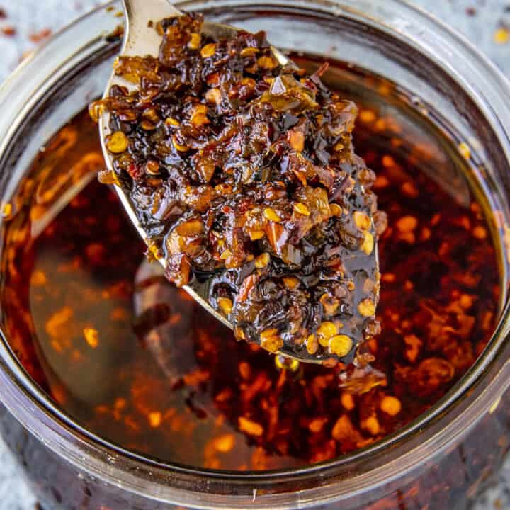 A spoonful of Homemade Spicy Chili Crisp rising from a glass jar