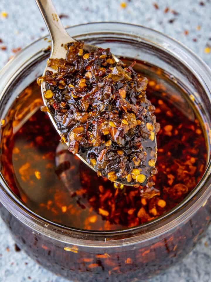 A spoonful of Homemade Spicy Chili Crisp rising from a glass jar