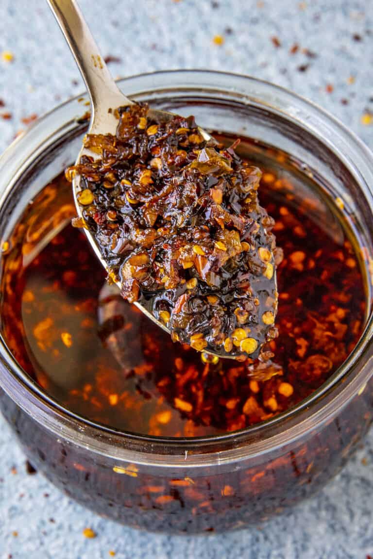 A spoonful of Homemade Spicy Chili Crisp rising from a glass jar