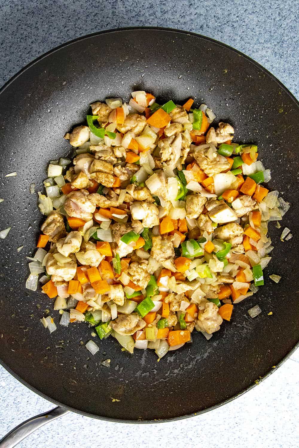 Cooking chopped chicken in a hot pan with peppers, onions and carrots