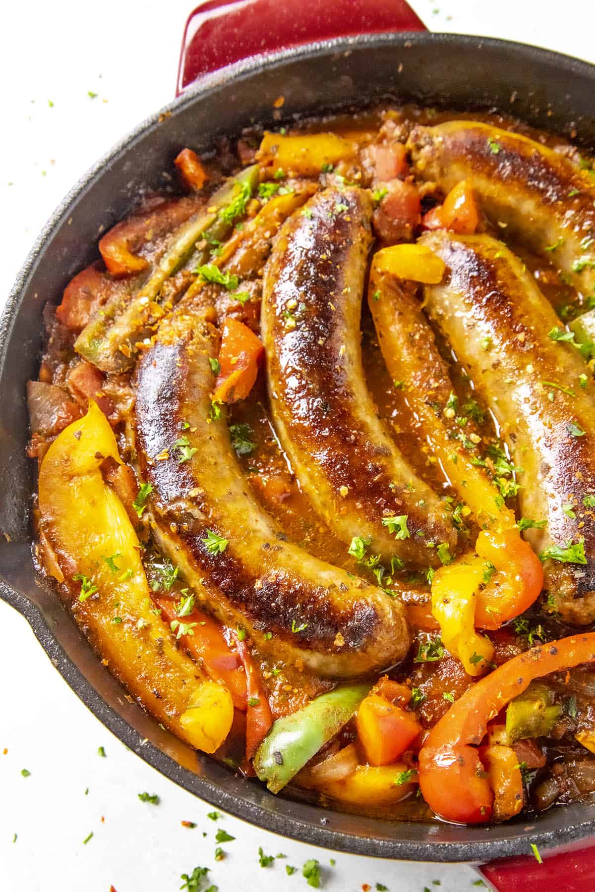 Sausage and Peppers in a hot pan with chili flakes and chopped green herbs.