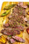 Sliced London broil on a cutting board with lots of grilled peppers