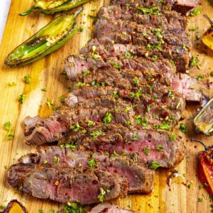 Sliced London broil on a cutting board with lots of grilled peppers