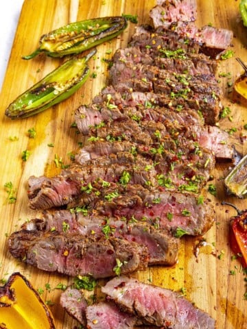 Sliced London broil on a cutting board with lots of grilled peppers