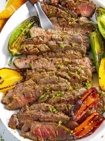 Serving sliced London broil on a platter with grilled peppers